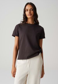 Zwarte katoenen t-shirt met opgerolde mouwen, ronde halslijn en subtiele logoprint op de borst, gecombineerd met crèmekleurige, losse broeken.