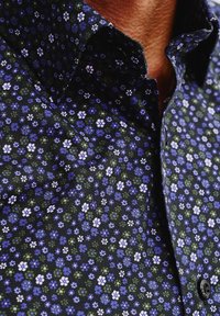 Granatowa koszula w kwiatowy wzór w bieli i odcieniach niebieskiego; posiada kołnierz rozpostarty oraz czarne guziki. Wykonana z bawełnianej tkaniny o gładkiej fakturze.