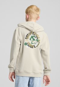 Felpa con cappuccio beige con tasca a marsupio, polsini e bordo a costine. Presenta una grafica colorata sul retro che raffigura un personaggio dei cartoni animati e del testo.