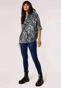Zwart-wit gestreepte top met oversized pasvorm en zijkoordjes, gecombineerd met donkerblauwe skinny jeans en zwarte enkellaarzen.