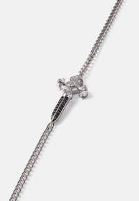 Colar em tom prateado com um pendente de cruz detalhado, realçado por gemas pretas e claras, design de corrente trançada e acabamento polido.