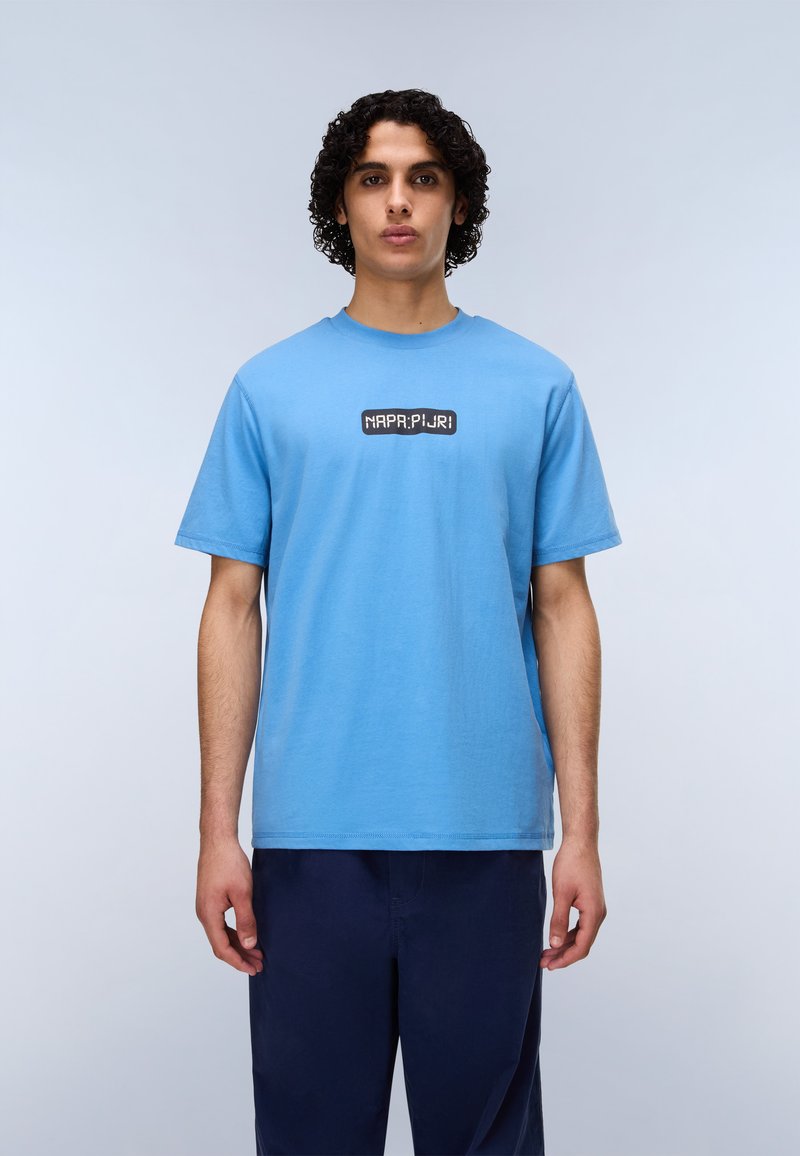 Ανοιχτό μπλε βαμβακερό μπλουζάκι με μαύρο ορθογώνιο λογότυπο και λευκό κείμενο μπροστά. Κοντά μανίκια και στρογγυλή λαιμόκοψη.