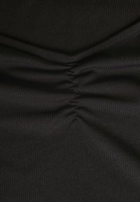 Svart tyg med vertikal ribbad textur, med draperingsdetaljer i mitten för extra formning. Slätt, lätt material.