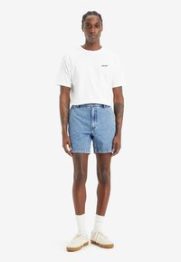 Tricou alb cu mânecă scurtă, având logo-ul "Levi's", combinat cu pantaloni scurți din denim de culoare albastru deschis, șosete albe și adidași bej. Outfit simplu și casual.