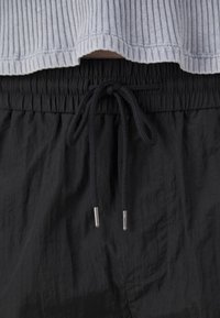 Shorts noirs avec taille élastique et cordon de serrage, en tissu texturé. La couche supérieure est un t-shirt côtelé bleu clair avec un design court.