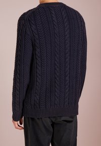 Marineblauer Strickpullover mit einem Kabelmuster und strukturierter Oberfläche. Verfügt über einen gerippten Halsausschnitt und Saum, von hinten auf einem schlichten Hintergrund zu sehen.