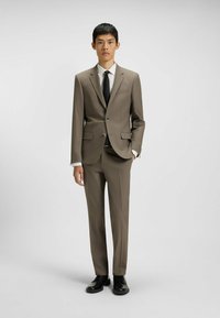 Beige suit with a tailored fit, single-breasted jacket, notched lapels, and two front pockets. Paired with a white shirt and black tie.