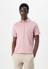 Light pink polo shirt with a collar and three button placket. Features a subtle brand logo embroidered on the chest. Short sleeves, casual fit.