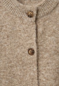 Beige Strickjacke mit geripptem Kragen, ausgestattet mit drei braunen Knöpfen und einem strukturierten, weichen Stoff. Einfaches Design mit einem klassischen Look.