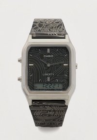 Digitale Casio-horloge met een zilverkleurige rechthoekige kast, een zwarte, gestructureerde band met een bloemenpatroon en een digitale display met tijdsaanduiding.