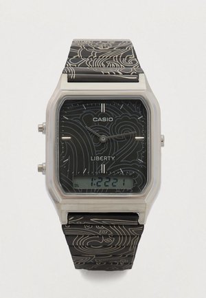 Digitális Casio óra ezüstszínű, téglalap alakú tokban, fekete, virágmintás texturált szíjjal, digitális kijelzővel az idő leolvasásához.