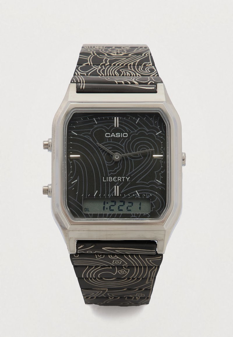 Digitale Casio-horloge met een zilverkleurige rechthoekige kast, een zwarte, gestructureerde band met een bloemenpatroon en een digitale display met tijdsaanduiding.