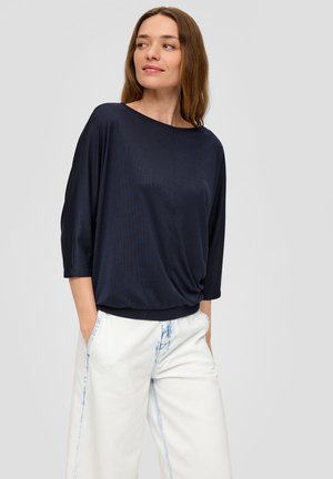 Donkerblauwe, lichte top met een losse pasvorm, brede halslijn en driekwartmouwen, gecombineerd met witte broek met lichte blauwe slijtage.
