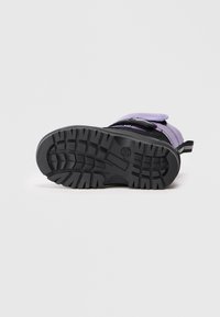 Botte violette imperméable avec semelle en caoutchouc noire. Elle dispose d'un motif de semelle texturé pour une meilleure adhérence et d'une sangle Velcro ajustable pour un maintien sécurisé.