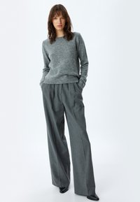 Maglione grigio lavorato a maglia con scollo rotondo abbinato a pantaloni grigi a pieghe larghi. L'outfit include scarpe nere con punta appuntita.