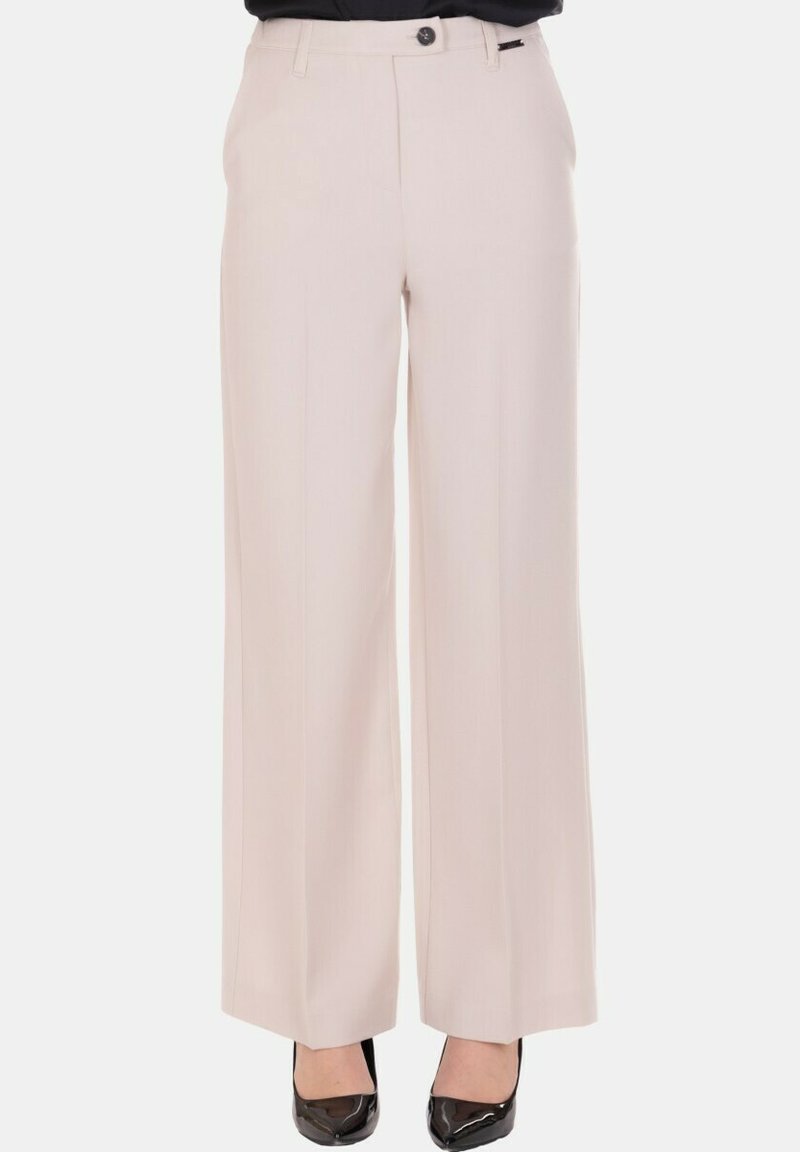 Pantaloni beige chiaro a gamba larga con piega frontale, chiusura con bottone e cerniera, indossati con décolleté nere con punta a spillo, mostrati dalla vita ai piedi.