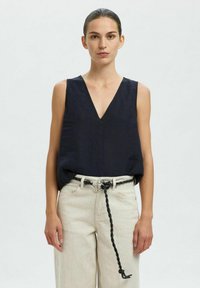 Haut sans manches en lin bleu marine avec un décollet�é en V prononcé, associé à un pantalon large beige clair et un détail de ceinture tressée noire.