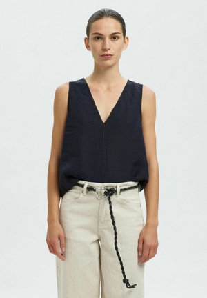 Navy linnen mouwloos topje met een diepe V-hals, gecombineerd met lichtbeige wijde broek en een gevlochten zwarte riemdetail.