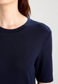 Granatowa koszulka z krótkim rękawem z okrągłym dekoltem, wykonana z miękkiego, elastycznego materiału, z subtelnymi detalami szycia wzdłuż szwów.