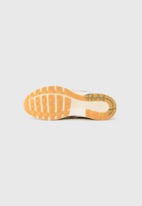 Podešev tenisky s oranžovým gumovým vzorkem, bílou střední podrážkou a vyraženým logem Nike poblíž paty na jednoduchém pozadí.