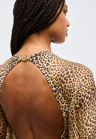 Γυναίκα με πλεξούδες που φοράει φόρεμα λεοπάρ με στρογγυλό χρυσό κούμπωμα και μεγάλο ανοιχτό πίσω μέρος.