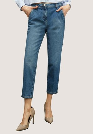 Jeans azules recortados de media altura con bolsillos delanteros, combinados con tacones altos de punta beige sobre un fondo claro.