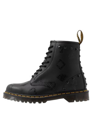 Czarny skórzany trzewik na sznurówki z tłoczonymi geometrycznymi wzorami, ozdobnymi ćwiekami, żółtym przeszyciem i oznaczoną taśmą do ściągania z tyłu.