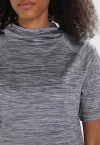 Top atlético gris hecho de tela texturizada, con cuello tipo mock, mangas cortas y un patrón sutilmente rayado en el material.