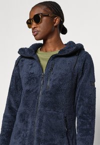 Giacca in pile navy con una texture morbida, con zip completa, cappuccio con cordino e due tasche laterali con zip, caratterizzata da una vestibilità rilassata.