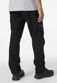 Zwarte waterdichte broek met taps toelopende benen, zijritsen en een logo-accent. Gemaakt van lichtgewicht en duurzaam materiaal. Geschikt voor buitenactiviteiten.