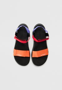 Sandales en caoutchouc noires avec des brides ajustables. Dotées de sangles orange, rouges et violettes, avec un logo blanc visible sur la bride orange.