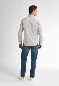 Camicia a maniche lunghe di un beige chiaro con motivo a pois neri, dotata di colletto e polsini con bottoni; abbinata a jeans in denim blu.