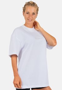 Witte oversized t-shirt met een ronde hals en korte mouwen, voorzien van subtiele geborduurde tekst aan de voorkant. Gemaakt van zachte stof.