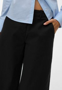 Pantalones anchos negros hechos de tela suave, con bolsillos delanteros, cintura ajustada y un acabado limpio en el dobladillo.