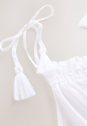 Top in cotone bianco con lacci regolabili con nappe, texture arricciata lungo lo scollo e design leggero e arioso.