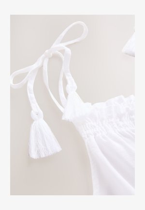 Top in cotone bianco con lacci regolabili con nappe, texture arricciata lungo lo scollo e design leggero e arioso.