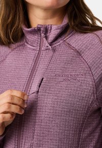 Veste en polaire violette avec un motif texturé, col zippé et logo brodé. Présente une poche zippée et une coupe ajustée.