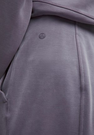 Lilla sportriietus, millel on sile tekstuur, väike reljeefne logo ja struktureeritud õmblused, mis on loodud mugavuse ja sobivuse tagamiseks.