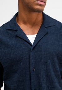 Marineblauwe short-sleeve shirt met een textuurpatroon, een pointe kraag en zwarte knopen, met een contrasterend wit onderhemd zichtbaar.