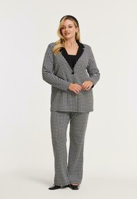 Zwart-wit pied-de-poule patroon pak met een blazer met een zwarte kraag en bijpassende wijde broek, gemaakt van gestructureerde stof.