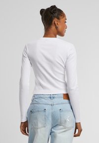 Hvit langermet crop topp med ribbet tekstur, kombinert med lyseblå høyt midje jeans med lommer og baklommer.