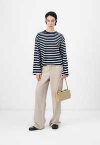 Camisa de rayas azul marino y blanca de manga larga, pantalones de pierna ancha beige y un pequeño bolso tan. Calzado negro con acentos texturizados.