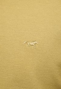 Tissu texturé beige avec un petit cheval courant brodé en fil beige assorti, centré sur la surface.