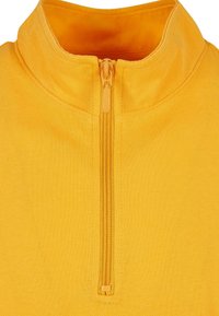 Gul zippered genser med høy krage, laget av strukturert stoff. Har matchende glidelås og sømmer, som viser en glatt finish.
