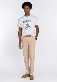 Camiseta blanca con el texto y gráfico en negro "HARPER", pantalones beiges y mocasines color caramelo. Diseño simple y casual, adecuado para entornos relajados.