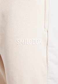 Lichtbeige stof met een textuur en een diagonaal ribpatroon. Het product heeft een subtiele geperste logo "SMILODOX" in een bijpassende kleur.