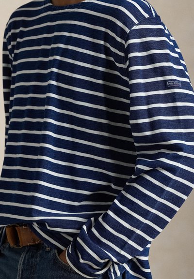 Μακρυμάνικο μπλουζάκι σε ναυτικό μπλε χρώμα με λευκές οριζόντιες ρίγες, κατασκευασμένο από απαλό ύφασμα. Διαθέτει στρογγυλή λαιμόκοψη και μικρό λογότυπο στο μανίκι.