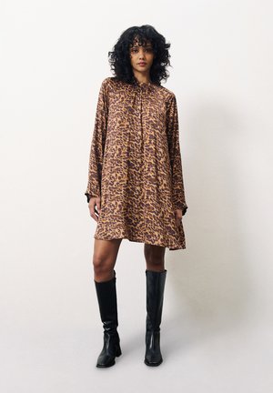 Tierdruckkleid in Braun und Beige, lockerer Schnitt mit langen Ärmeln, rundem Ausschnitt und leicht ausgestelltem Schnitt, kombiniert mit schwarzen knielangen Stiefeln.