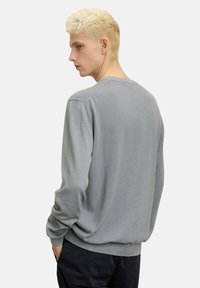 Maglione grigio a maniche lunghe con scollo rotondo e polsini a coste. Texture morbida, vestibilità rilassata e dettaglio di cuciture minimal sulle spalle.