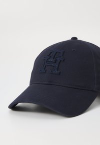 Navy blue baseball cap with embroidered logo, curved brim, and structured front. Made from a textured fabric; features ventilation holes on the crown.
